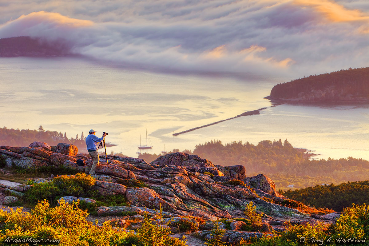 A man tries to photograph Bar Harbor, Maine at sunrise from Cadillac Mountain.