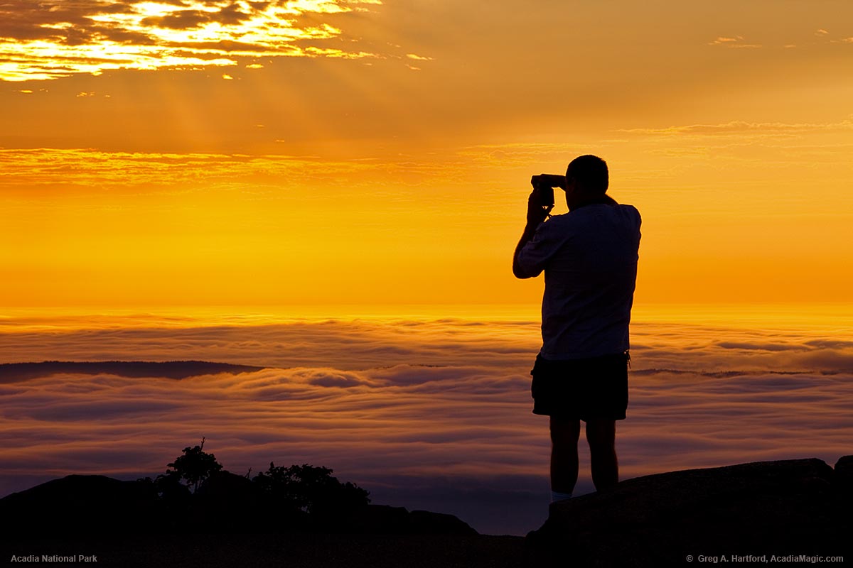 A park visitor photographs the sunrise from Cadillac Mountain in Acadia National Park.