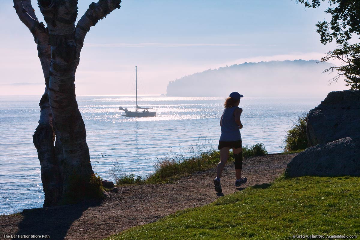 A woman is jogging on the Bar Harbor Shore Path.