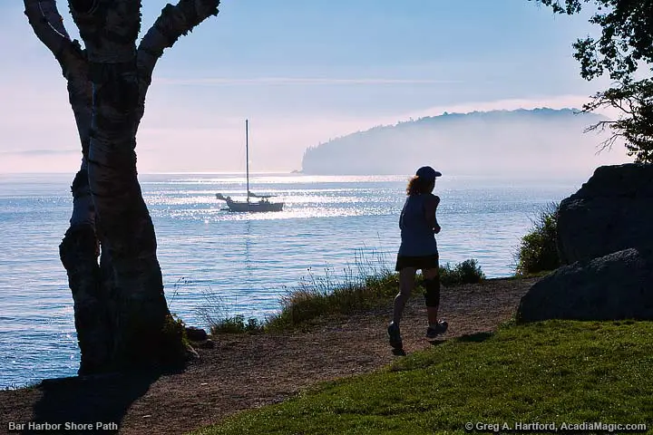 A woman jogs on the Shore Path in the morning with yacht in the distance