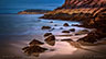 A beautiful misty sunrise at Sand Beach in Acadia National Park with Otter Cliff in the distance